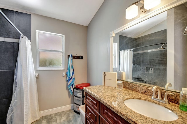 bathroom with vaulted ceiling, a tile shower, vanity, and baseboards