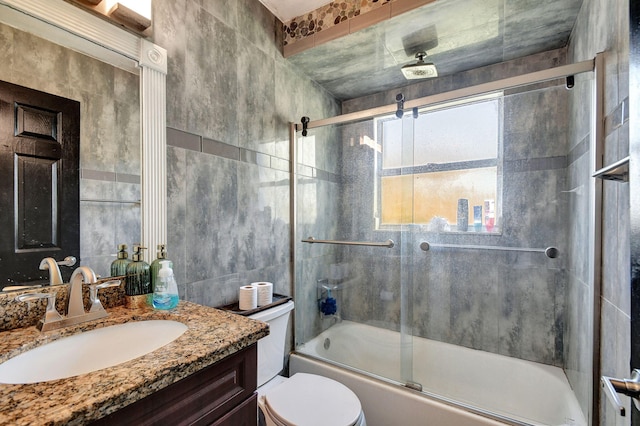 full bathroom featuring toilet, combined bath / shower with glass door, vanity, and tile walls