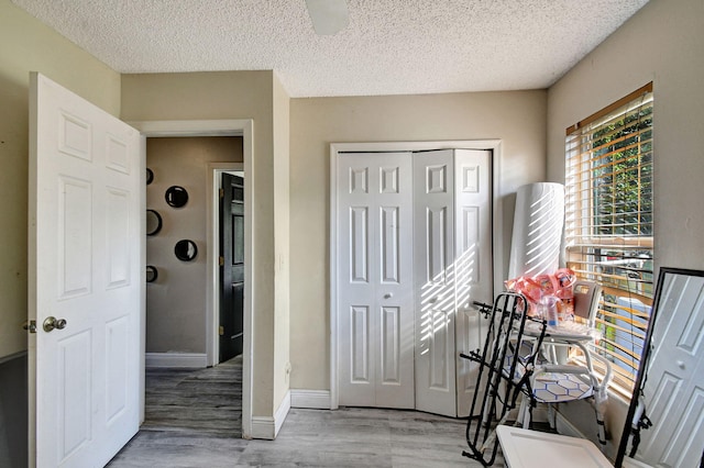 interior space with a closet, a ceiling fan, a textured ceiling, wood finished floors, and baseboards