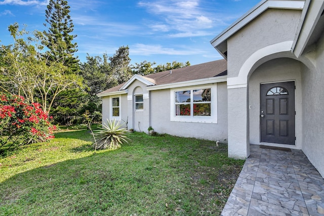 doorway to property featuring roof with shingles, a lawn, and stucco siding