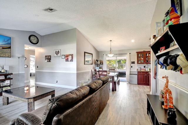 living room featuring baseboards, visible vents, vaulted ceiling, a textured ceiling, and light wood-type flooring