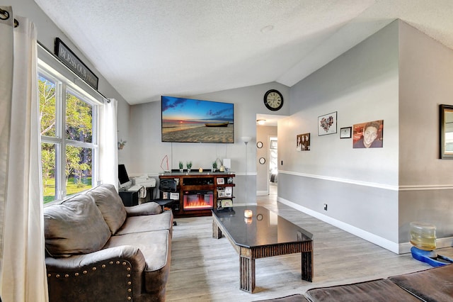 living room featuring lofted ceiling, a textured ceiling, baseboards, and wood finished floors