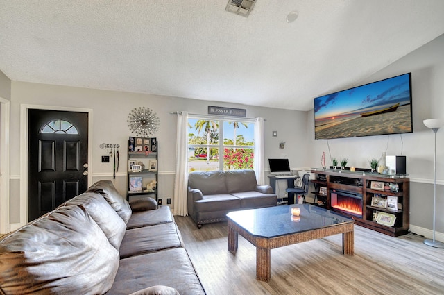 living area featuring a textured ceiling, a glass covered fireplace, visible vents, and light wood-style floors