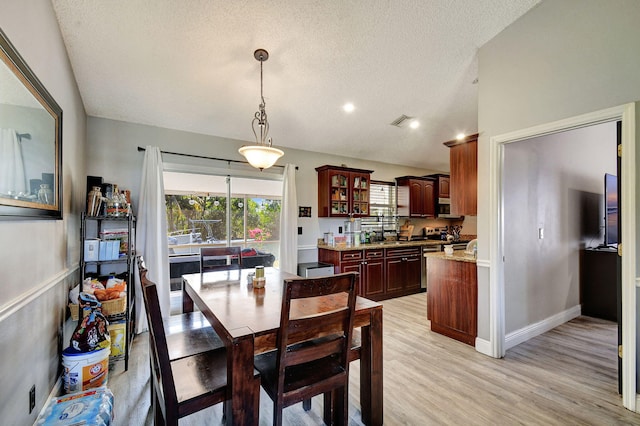 dining room featuring a textured ceiling, light wood-style flooring, visible vents, baseboards, and vaulted ceiling