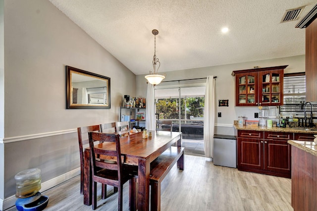 dining room with light wood finished floors, visible vents, vaulted ceiling, and a textured ceiling