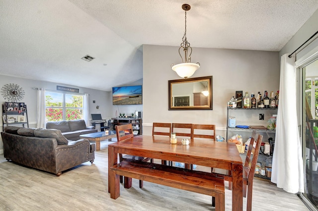 dining space featuring a wealth of natural light, light wood-type flooring, visible vents, and vaulted ceiling