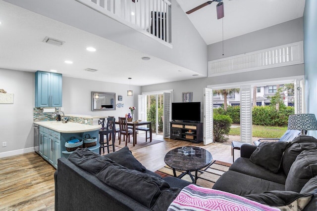 living room with ceiling fan, a towering ceiling, light hardwood / wood-style flooring, and a wealth of natural light