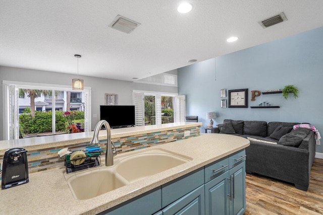 kitchen with decorative light fixtures, blue cabinets, sink, light hardwood / wood-style floors, and a textured ceiling