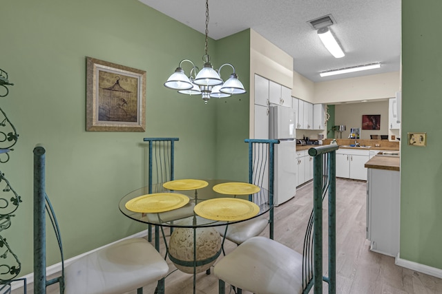 dining room featuring a notable chandelier, sink, a textured ceiling, and light wood-type flooring