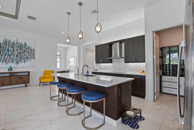 kitchen featuring pendant lighting, sink, a kitchen island with sink, black electric cooktop, and wall chimney exhaust hood