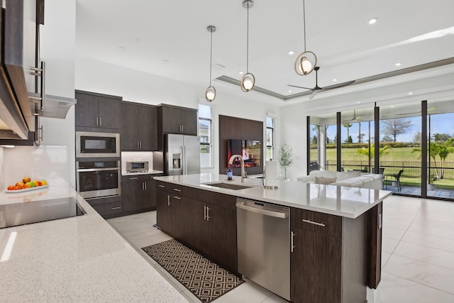 kitchen featuring sink, dark brown cabinets, appliances with stainless steel finishes, an island with sink, and pendant lighting