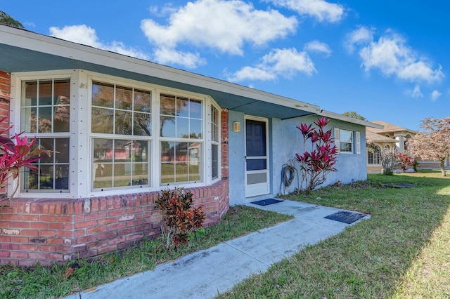 entrance to property with brick siding, a lawn, and stucco siding