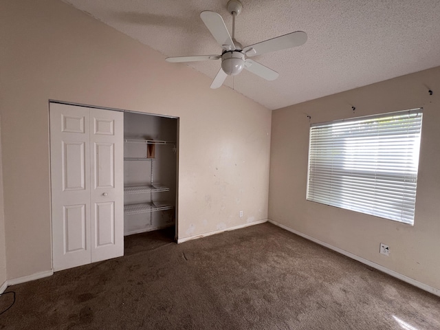 unfurnished bedroom with vaulted ceiling, dark carpet, ceiling fan, a textured ceiling, and a closet