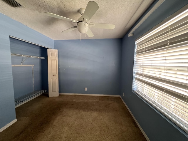 unfurnished bedroom with dark carpet, a textured ceiling, a closet, and ceiling fan