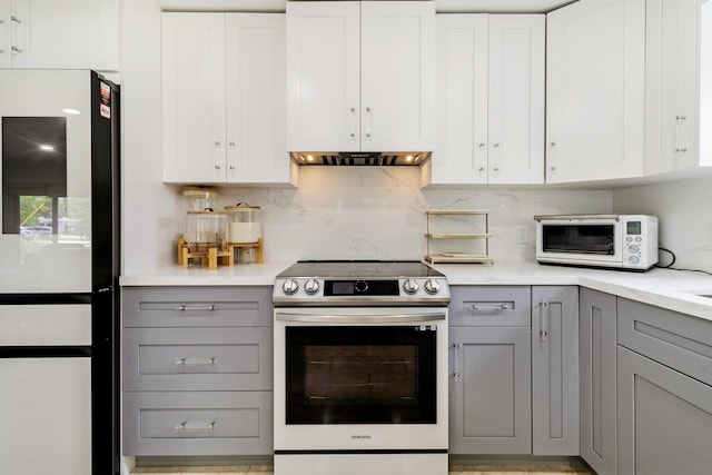 kitchen with gray cabinetry, white cabinetry, stainless steel electric range, fridge, and backsplash