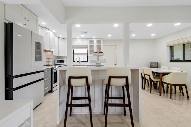 kitchen with white cabinetry, a breakfast bar area, fridge, and stainless steel range with electric stovetop