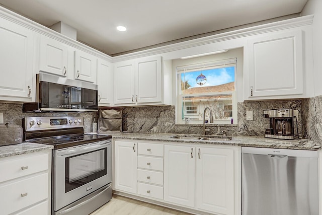 kitchen with light stone counters, stainless steel appliances, sink, and white cabinets