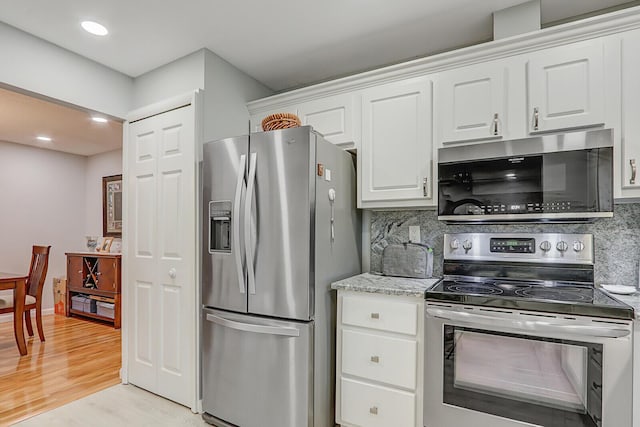 kitchen with tasteful backsplash, stainless steel appliances, light hardwood / wood-style floors, and white cabinets