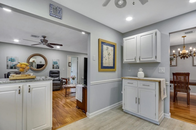 kitchen featuring hanging light fixtures, white cabinetry, ceiling fan with notable chandelier, and light hardwood / wood-style floors