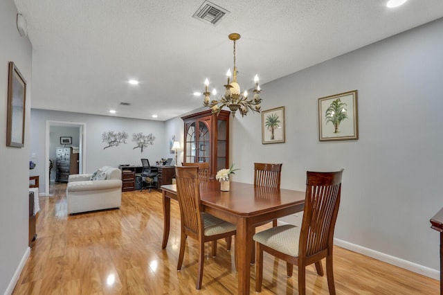 dining space with an inviting chandelier, a textured ceiling, and light wood-type flooring