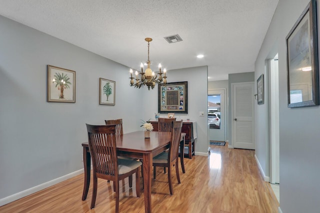 dining area with a chandelier, light hardwood / wood-style floors, and a textured ceiling