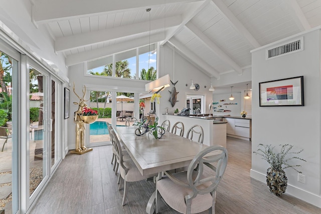 dining space with beam ceiling, high vaulted ceiling, and light wood-type flooring