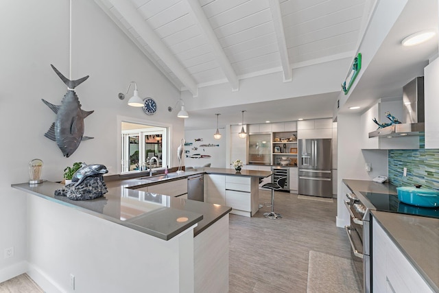 kitchen with pendant lighting, white cabinetry, stainless steel appliances, kitchen peninsula, and wall chimney exhaust hood