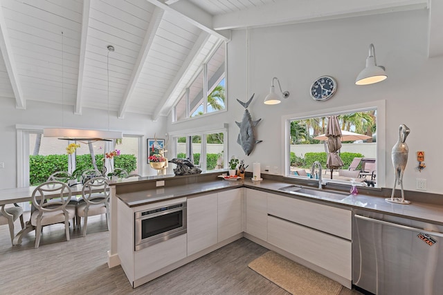 kitchen featuring sink, kitchen peninsula, stainless steel appliances, beam ceiling, and hardwood / wood-style floors