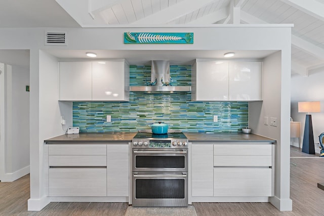 kitchen with ventilation hood, white cabinetry, tasteful backsplash, and range with two ovens