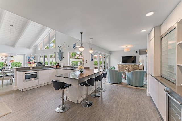 kitchen featuring vaulted ceiling with beams, pendant lighting, stainless steel microwave, and light hardwood / wood-style flooring