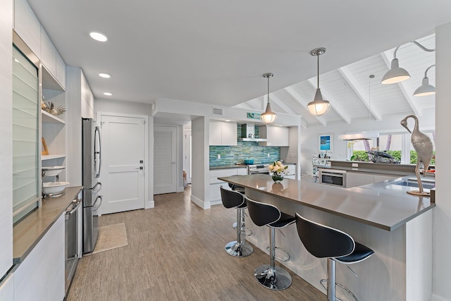 kitchen featuring tasteful backsplash, vaulted ceiling with beams, white cabinets, a kitchen breakfast bar, and hanging light fixtures