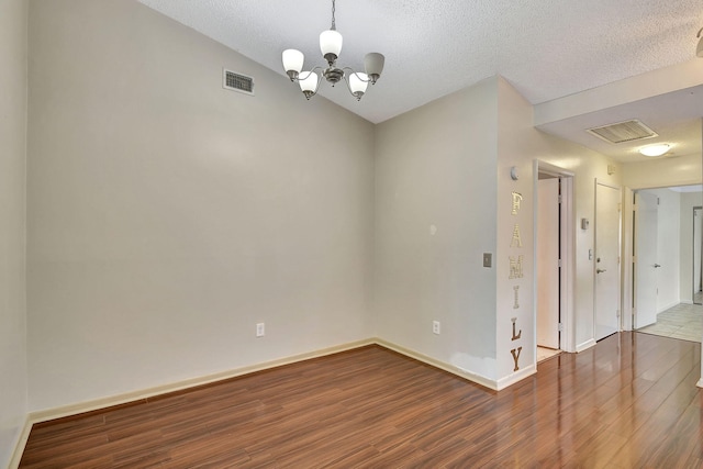 unfurnished room featuring hardwood / wood-style flooring, vaulted ceiling, an inviting chandelier, and a textured ceiling