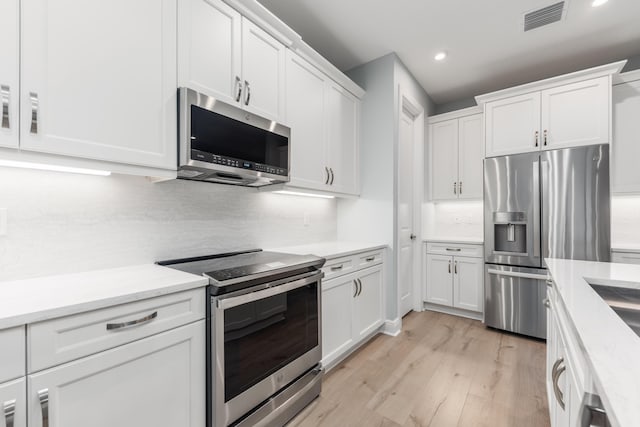 kitchen featuring white cabinetry, decorative backsplash, light wood-type flooring, and appliances with stainless steel finishes