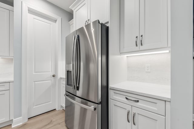 kitchen featuring tasteful backsplash, white cabinetry, light stone counters, stainless steel refrigerator with ice dispenser, and light wood-type flooring