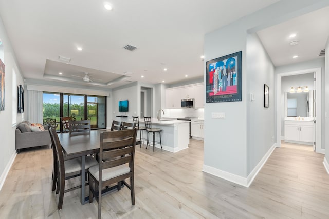 dining area featuring ceiling fan, a raised ceiling, and light hardwood / wood-style flooring