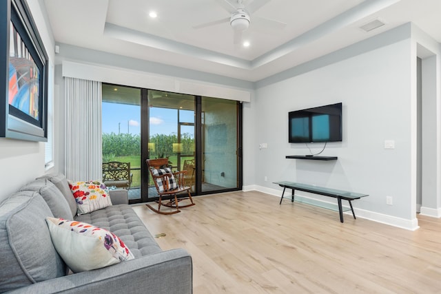 living room with ceiling fan, a tray ceiling, and light hardwood / wood-style flooring