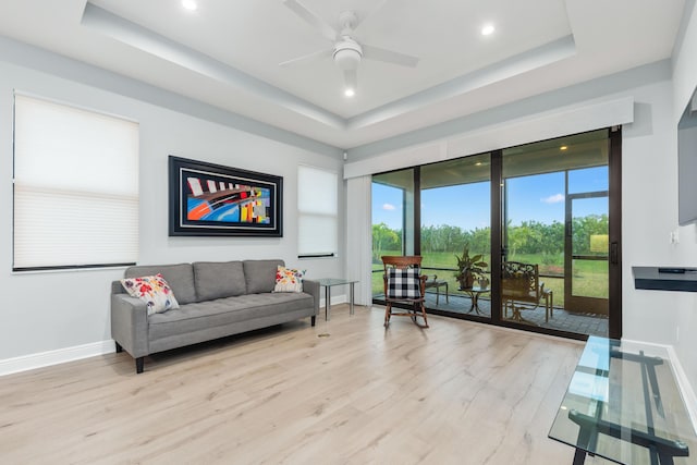 living room with ceiling fan, a wealth of natural light, light hardwood / wood-style floors, and a tray ceiling