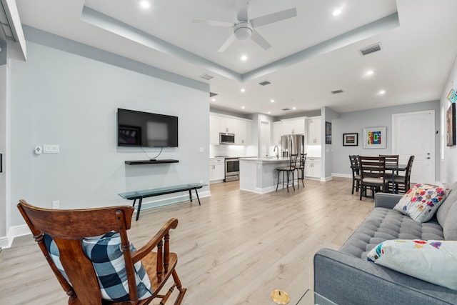 living room featuring a tray ceiling, ceiling fan, and light wood-type flooring