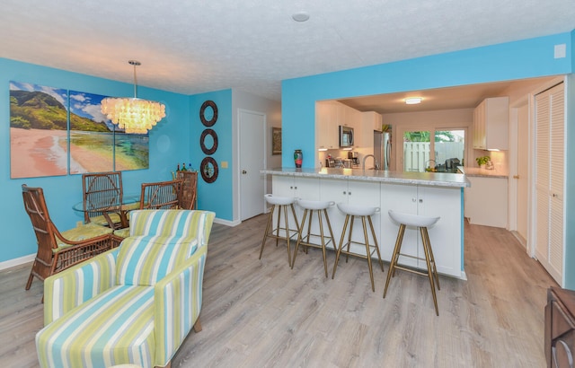 kitchen with white cabinetry, light hardwood / wood-style flooring, appliances with stainless steel finishes, kitchen peninsula, and pendant lighting