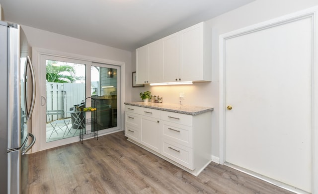 kitchen featuring stainless steel refrigerator, hardwood / wood-style floors, light stone counters, and white cabinets