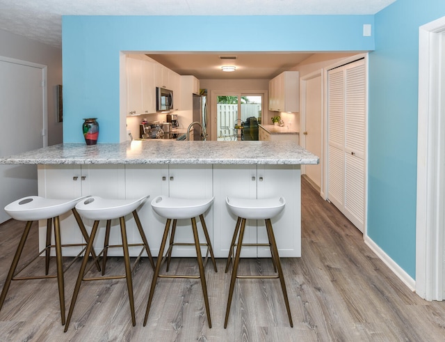 kitchen with a breakfast bar, white cabinetry, stainless steel appliances, light stone counters, and kitchen peninsula