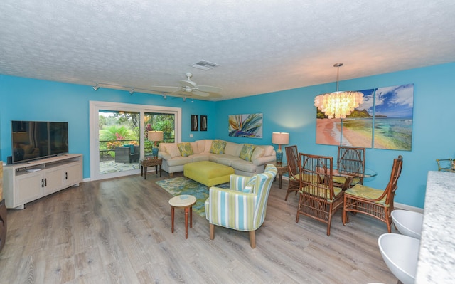 living room featuring ceiling fan with notable chandelier, light hardwood / wood-style flooring, and a textured ceiling