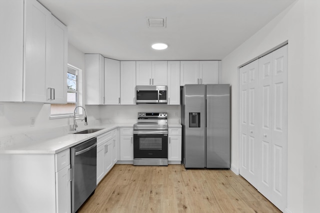 kitchen with appliances with stainless steel finishes, white cabinetry, sink, light stone countertops, and light hardwood / wood-style flooring