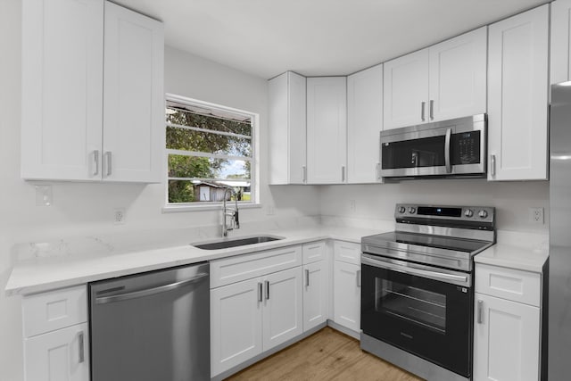 kitchen featuring appliances with stainless steel finishes, sink, white cabinets, and light hardwood / wood-style flooring