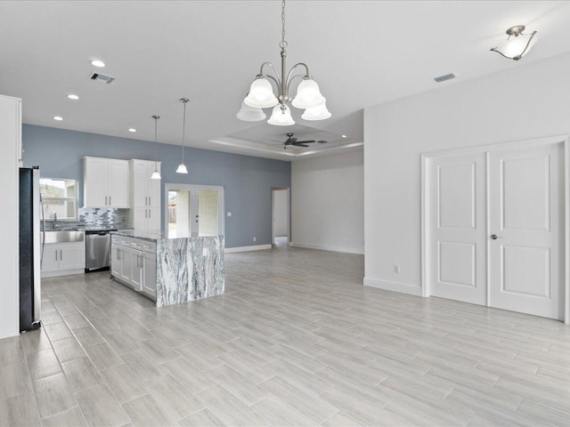 kitchen featuring appliances with stainless steel finishes, pendant lighting, light stone countertops, ceiling fan with notable chandelier, and white cabinets