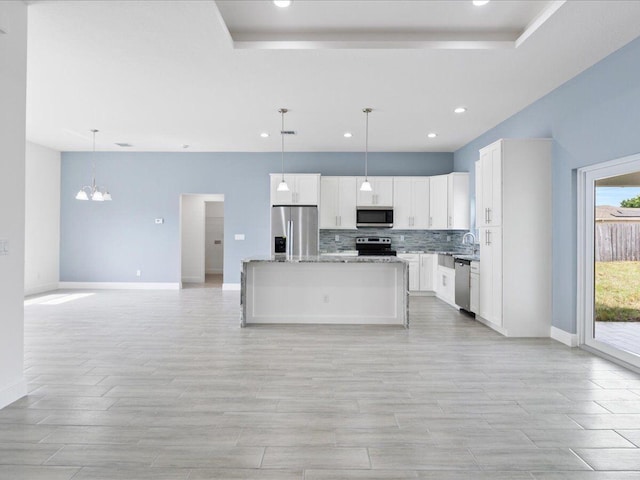 kitchen with white cabinetry, a center island, appliances with stainless steel finishes, pendant lighting, and light stone countertops