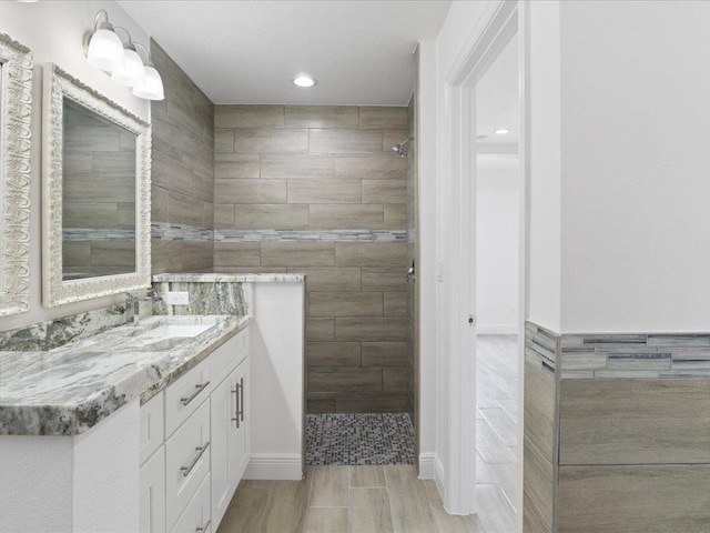 bathroom with tiled shower, vanity, and tile walls