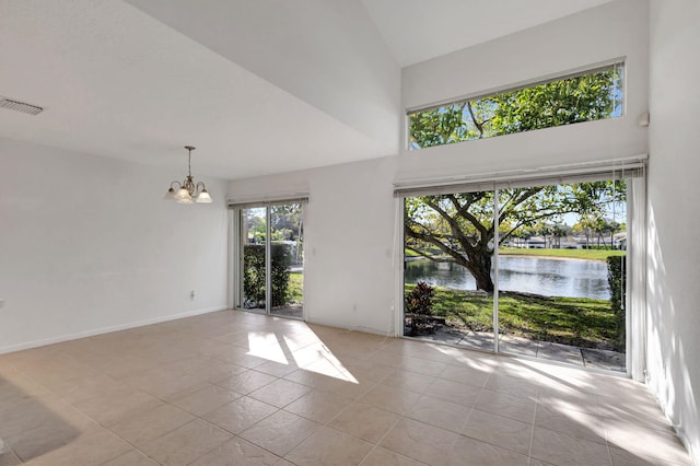 empty room featuring light tile patterned flooring, a water view, a towering ceiling, and a notable chandelier