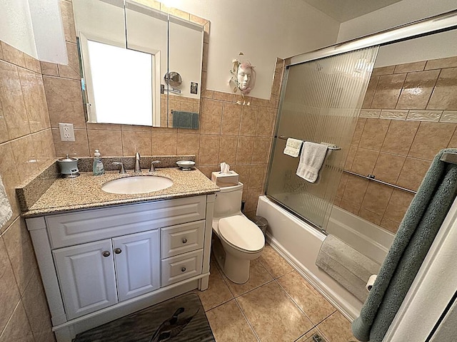 full bathroom featuring tile patterned floors, toilet, combined bath / shower with glass door, tile walls, and vanity