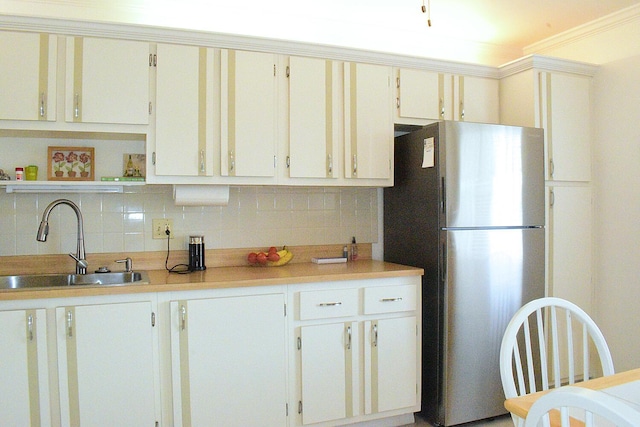 kitchen with white cabinetry, sink, decorative backsplash, and stainless steel fridge